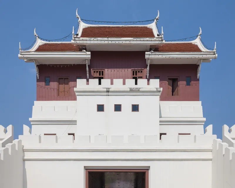 White crenellated Chum Phon Gate with red timber upper walls and three tiled roof sections.